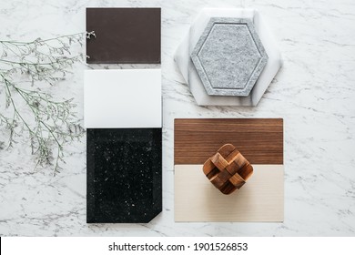 Top View Of Material Sample Selections Including Granite Tile, Marble Tile, Acoustic Tile, Walnut And Ash Wood Laminate With Plant On Marble Top Table.