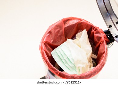 Top View Medical Gloves, Dispose Mask And Infectious Waste In Red Plastic Bag Infection Bin On White Floor Background.