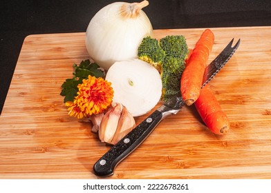 top view, medium distance of  fresh Provence vegetables of; broccoli, white onion, carrots, shallots and serrated knife with three chrysanthemums blooms