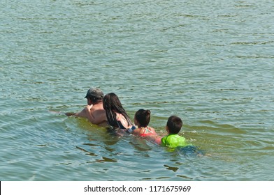 Top View, Medium Distance Of A Hispanic Family Swimming , By Holding On To Each Other And Father Pulling Them Through Tropical Water Of The Gulf Of Mexico, On A Sunny, Summer Day
