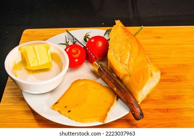 Top View, Medium Distance Of, A French Baguette, White Ramekin Of Butter, Two Cherry Tomatoes And A Slice Of Cheese, On A White Plate, On A  Wood Serving Board