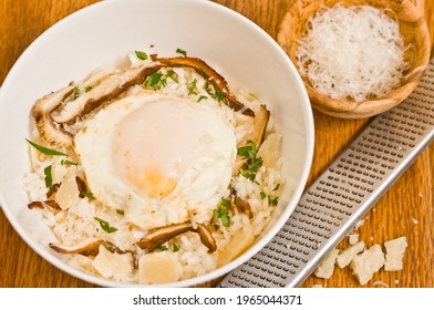 Top View, Medium Distance Of A Round, White, Bowl Of Mushroom Risotto With A Sunny Side Up Egg And A Bowl Of Cheese 