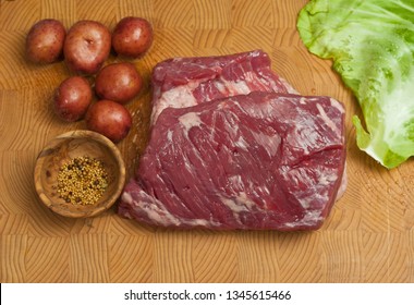 Top view, medium distance, three pound, raw, corn beef brisket, six small, red, potatoes, wood, rare bowl of dill, leaf of cabbage, bamboo, wood, cutting board ingredients for, St patrick's day dinner