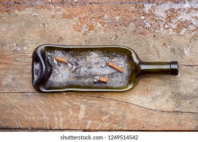 Top View Of A Melted Wine Bottle Ashtray On Wooden Weathered Background, With Snow Snow In Corner. 