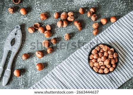 Top view of metal nutcracker, scattered filberts and fringed kitchen towel on gritty dark surface, rustic Nordic styling, perfect banner for healthy snacking ads