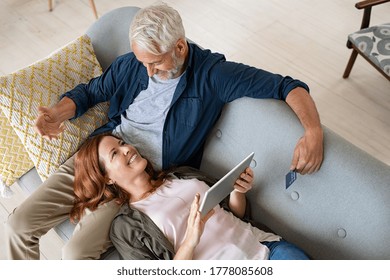 Top view of middle aged couple booking holidays online with a credit card. High angle view of mature woman lying on old man lap using digital tablet to buy on an ecommerce website, shopping online. - Powered by Shutterstock