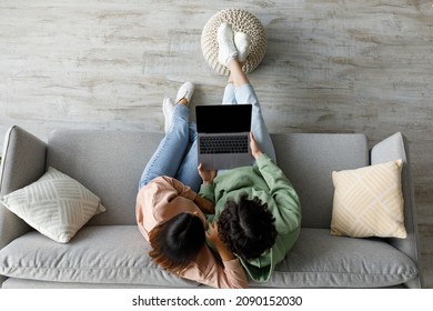 Top view of millennial Asian couple sitting on couch with laptop at home, mockup for website design on pc screen. Young spouses browsing web, watching movie together, space for online ad