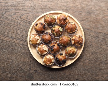 Top View Mini Banana Muffins With Sesame, Raisin, Cranberry, Macadamia And Pumpkin Seed Topping On Wooden Plate