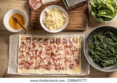 Top view of the mini pizza cake preparation process. Bacon stacked on puff pastry, next to spinach, grated cheese and egg - Top of view. Recipe procedure: 2 of 10