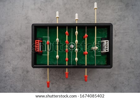 Top view of mini table football game with an old black and white soccer ball. On a gray background with shadows. Play game during home quarantine for Coronavirus.
