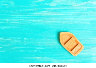 Top View Of A Miniature Toy Boat Placed On A Turquoise Wooden Table Background Imitating Sea.