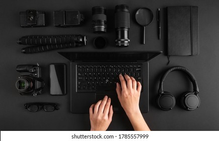 Top view of minimal photographers desk. Female hands working on laptop. Black photography gear flat lay.