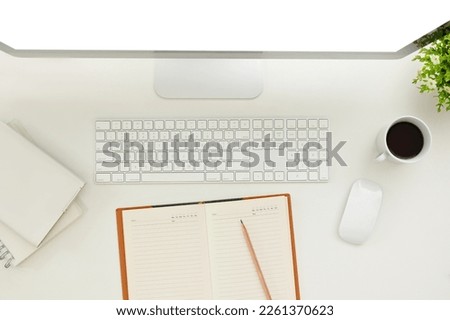 Top view of a minimal white office desk workspace with computer, keyboard, mouse, coffee cup, pencil and book with empty pages.