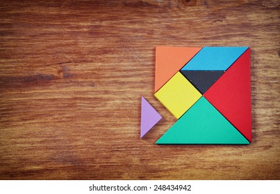 top view of a missing piece in a square tangram puzzle, over wooden table.