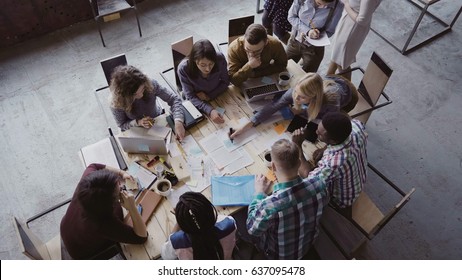 Top view of mixed race business team sitting at the table at loft office and working. Woman manager brings the document.
