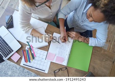 Top view of mixed race teen girl doing math task, school homework together with female teacher in the living room at home