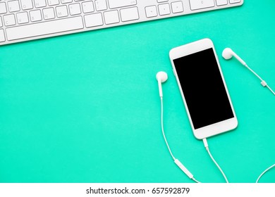 Top View Of Mobile Phone With Headphone And White Keyboard On Fresh Green Background