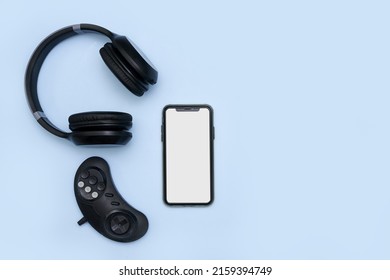 A Top View Of A Mobile Phone, Joystick And Headphones Over The Blue Surface