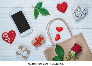 Top View Of Mobile Phone And St. Valentine's Day Mother's Day, 8th Of March Decorations, Paper Gift Bag And Rose Flowers.  Flatlay Background. Online Shopping, Holiday Sale Concept.