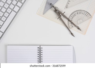 Top View Mock Up Of A White Drafting Table With Computer Keyboard, Compass, Protractor And Angle Open Notebook And Graph Paper. Horizontal Format With Copy Space.