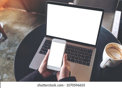 Top View Mockup Image Of Hands Holding Blank Mobile Phone While Using Laptop With Blank White Desktop Screen On Table 