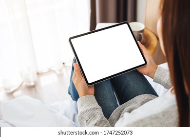 Top View Mockup Image Of A Woman Holding Black Tablet Pc With Blank Desktop White Screen While Sitting On A Cozy White Bed At Home