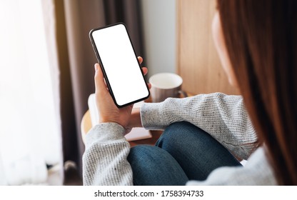 Top View Mockup Image Of A Woman Holding Mobile Phone With Blank Desktop Screen While Sitting In Bed Room At Home