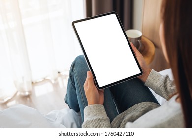 Top view mockup image of a woman holding black tablet pc with blank desktop white screen while sitting on a cozy white bed at home - Powered by Shutterstock