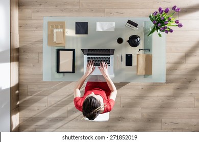 Top View, Modern Businesswoman Sitting At Glass Desk And Working On Her Laptop, Her Table Is Perfectly Tidy, The Sun Casts Graphics Shadows On The Wood Floor