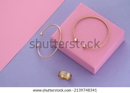Top view of modern golden bracelets and ring on pink podium on purple background with copy space