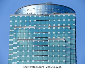 Top view of a modern high-rise building with green windows and an additional large blue cylindrical building on the roof. - Powered by Shutterstock