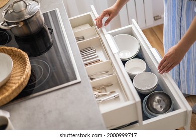 Top view modern housewife tidying up kitchen cupboard during general cleaning or tidying up. Female neatly placing dishware and cutlery in drawer of table. Storage organization Konmati method