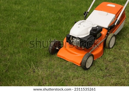 Top view of modern orange-grey electric lawn mower cutting bright lush green grass. Gardening work tools. Rotary lawn mower machine on lawn. Professional lawn care service. Place for text.