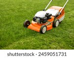 Top view of modern orange-grey gasoline lawn mower cutting bright lush green grass. Gardening work tools. Rotary lawn mower machine on lawn. Professional lawn care service. Place for text.