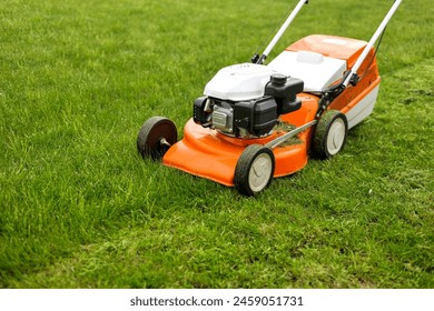 Top view of modern orange-grey gasoline lawn mower cutting bright lush green grass. Gardening work tools. Rotary lawn mower machine on lawn. Professional lawn care service. Place for text. - Powered by Shutterstock