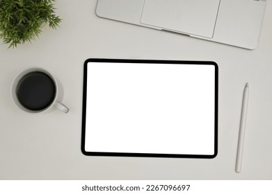 Top view of a modern workspace with digital tablet touchpad white screen mockup, stylus pen, laptop, coffee cup and decor plant on white background.