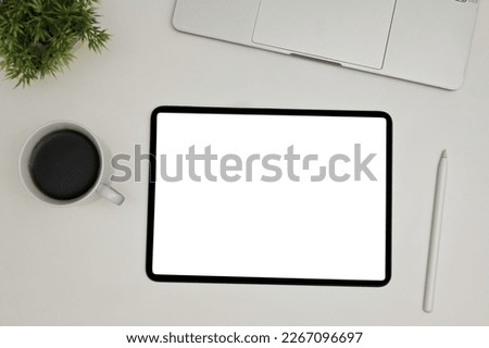 Top view of a modern workspace with digital tablet touchpad white screen mockup, stylus pen, laptop, coffee cup and decor plant on white background.