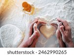 Top view of mom and daughter hands making dough heart for cookies at home domestic kitchen. Close up image of females hands making sign in the shape of heart during baking process