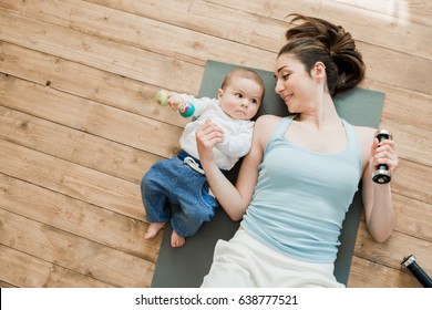Top view of mother with baby boy lying on floor and playing with dumbbells 