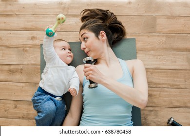 Top view of mother with baby boy lying on floor and playing with dumbbells 