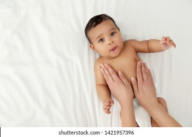 Top view of mother and her cute child on white bed, space for text. Baby massage and exercises