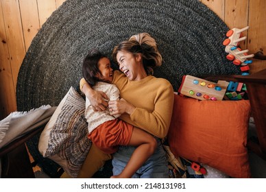 Top view of a mother and her daughter laughing cheerfully at home. Happy mother and daughter lying on the floor in their play area. Mother and daughter spending some quality time together.