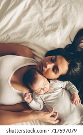 Top View Of Mother And Son Sleeping Together On Bed. Young Woman With A Newborn Baby Boy In The Bed At Home.