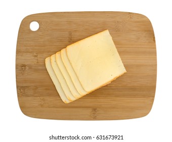 Top View Of Muenster Cheese Slices Stacked On A Wood Cutting Board Isolated On A White Background.