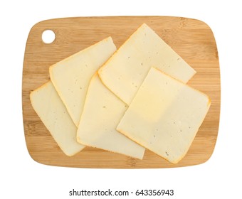 Top View Of Muenster Cheese Slices On A Wood Cutting Board Isolated On A White Background.