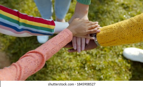Top view of multiethnic family putting hands together outdoors. Close up of happy parents and children stack of hands over green grass background. Family unity and trust concept