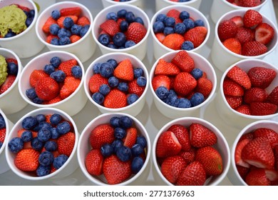 Top view of multiple plastic cups filled with fresh strawberries and blueberries. Concept of wholesale berry market, healthy diet nutrition, and vibrant organic food display