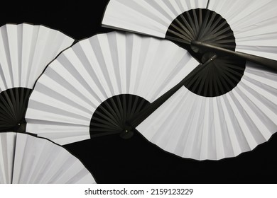 A top view of multiple white hand fans on the black surface