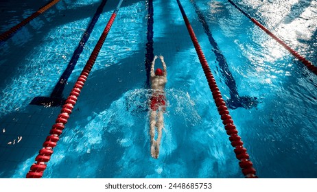 Top view of muscular, athletic young man, swimmer in red cap in motion, showing strength, training, swimming in pool indoors. Concept of professional sport, health, endurance, active lifestyle - Powered by Shutterstock