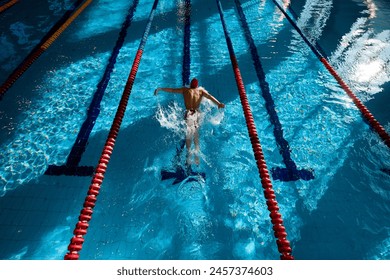 Top view of muscular, athletic young man, swimmer in red cap in motion, showing strength, training, swimming in pool indoors. Concept of professional sport, health, endurance, active lifestyle - Powered by Shutterstock